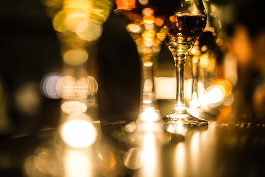 Row of wine glasses with amber-colored liquid on a dimly lit bar, with warm bokeh lights creating a moody, elegant atmosphere.