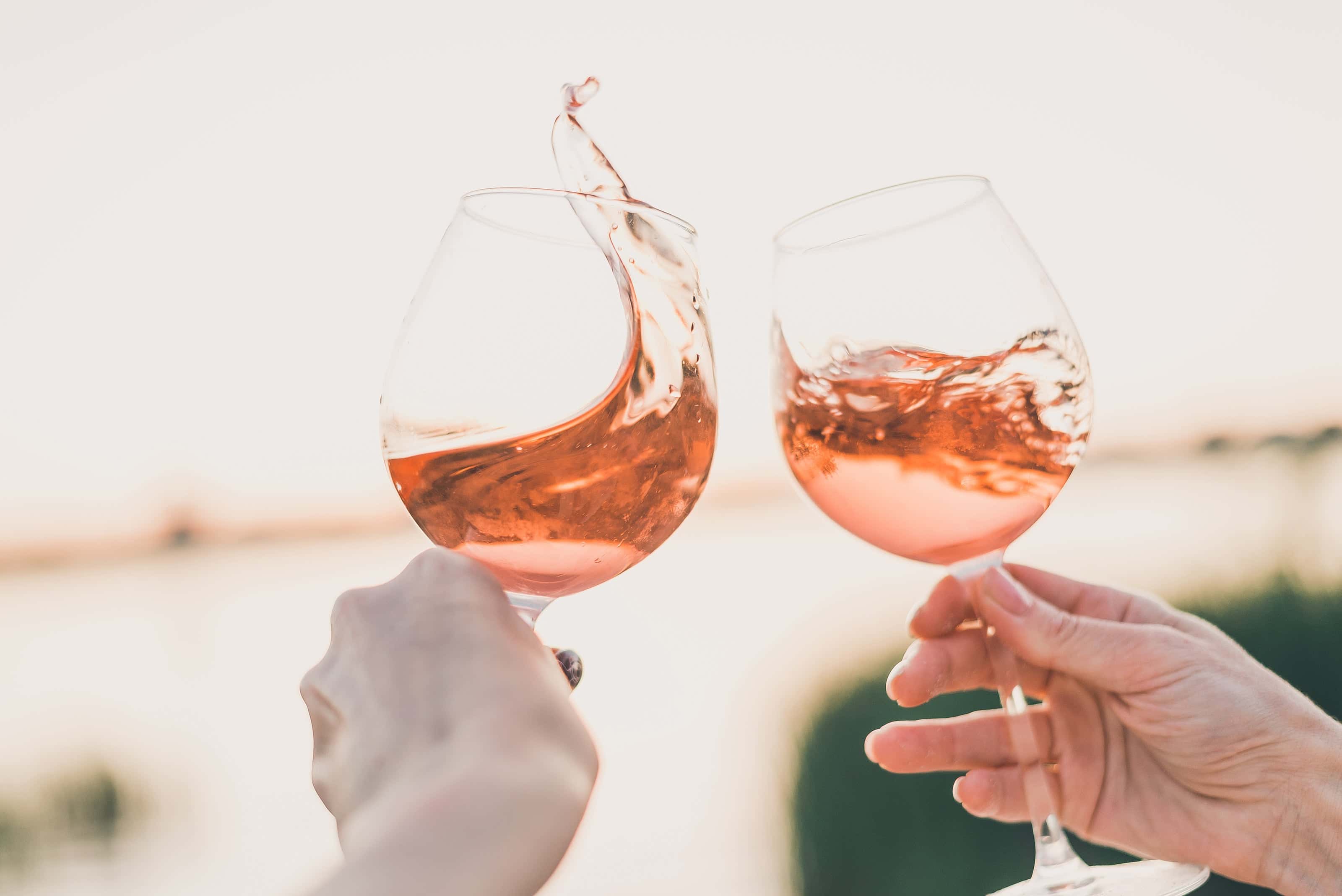 Two people clinking glasses of rosé wine with vibrant splashes, celebrating outdoors at sunset.