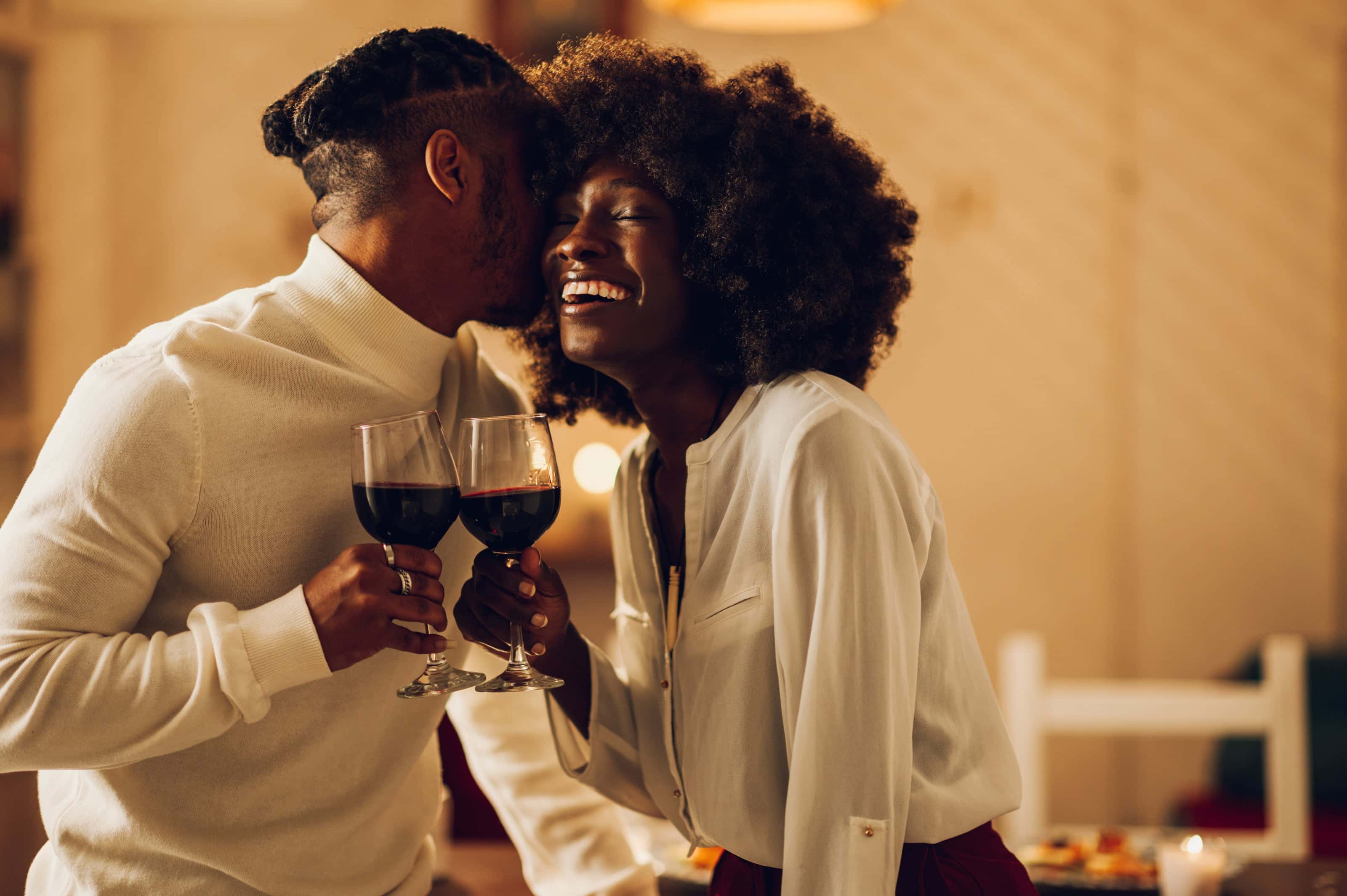 Romantic couple sharing a moment with glasses of red wine during a cozy evening at home.