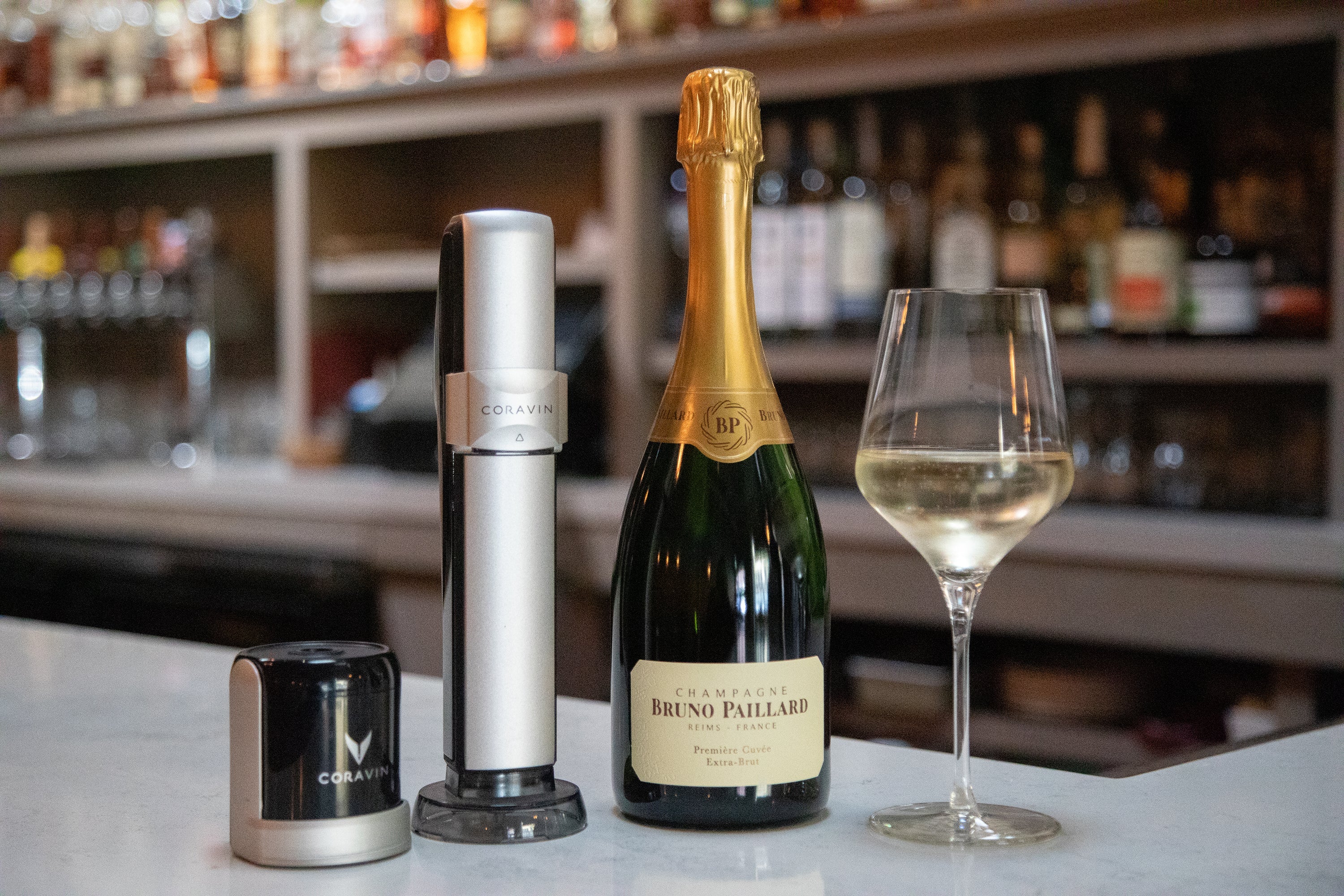 Coravin Sparkling wine preservation system with Bruno Paillard Champagne bottle and glass of sparkling wine on bar counter.