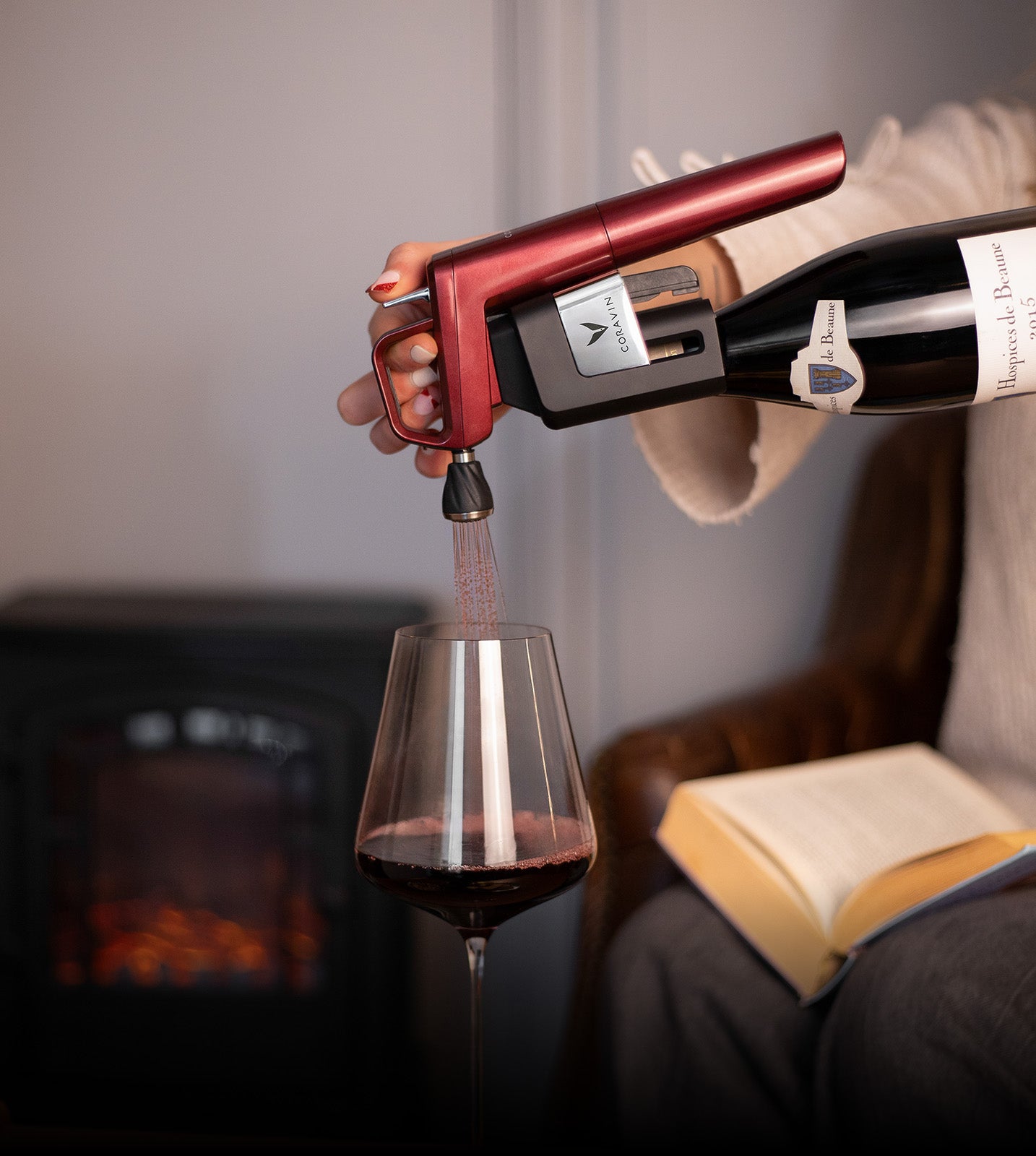 Person using a wine opener to pour red wine into a glass with a cozy indoor background.