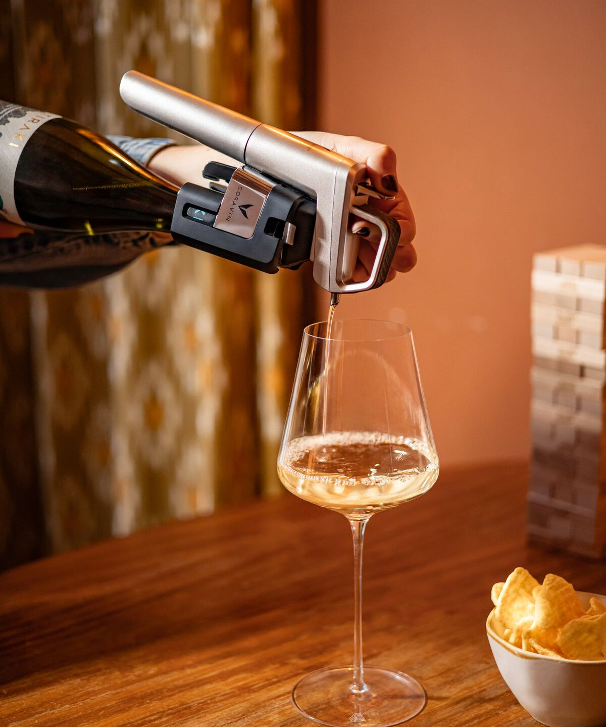 Person opening a bottle of wine with a coravin timeless pouring it into a glass on a wooden table with chips.